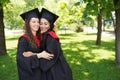 Successful graduates in academic dresses looking at camera and smiling outdoors in green park, place for text