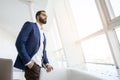 Successful handsome businessman in a blue suit stands against the background of a white office and looks out the window, portrait Royalty Free Stock Photo
