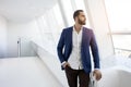 Successful handsome businessman in a blue suit stands against the background of a white office and looks out the window, portrait Royalty Free Stock Photo