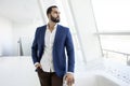 Successful handsome businessman in a blue suit stands against the background of a white office and looks out the window, portrait Royalty Free Stock Photo