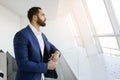 Successful handsome businessman in a blue suit at the workplace looks out the window, portrait of a manager at work