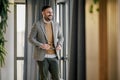 Successful happy entrepreneur in formals looking through window at office