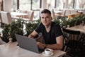 Successful happy young business man in a black t-shirt with a modern computer sits in a vintage cafe. Joyful freelancer guy Royalty Free Stock Photo