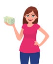 Successful happy young business woman holding cash / money / currency / banknote bundle in hand and holding another hand on hip.