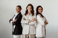 Successful international young businesswomen posing with arms crossed and smiling at camera, standing over light wall Royalty Free Stock Photo