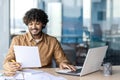 Successful and joyful financier accountant works with papers and documents inside office at workplace, businessman reads