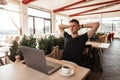 Successful joyful young business man in a black t-shirt with a computer sits in a modern cafe. Happy freelancer guy working Royalty Free Stock Photo