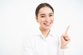 Successful korean businesswoman, pointing finger right, showing advertisement on banner, standing over white background