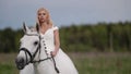 A successful lady riding a white posh horse gallops across a field in a white dress