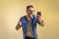 Successful male freelancer reading good news over mobile phone and screaming cheerfully against beige background. Young man Royalty Free Stock Photo