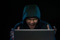 Successful male hacker poses in front of laptop computer, clenches fists, dressed in black clothes, rejoices finishing bad data