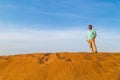 The successful man with a beard in a blue t-shirt costs at dune barkhan top in the desert At a backgr Royalty Free Stock Photo