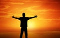 A successful man celebrating victory while standing on a mountain with sunset background Royalty Free Stock Photo
