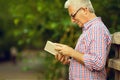 Successful man concept. Profile portrait of a smiling happy mature (old) man in trendy casual shirt & glasses reading book in Royalty Free Stock Photo