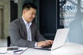 Successful mature asian working inside office using laptop, man typing on keyboard and smiling, businessman satisfied Royalty Free Stock Photo