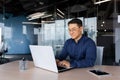 Successful mature asian working inside office using laptop, man typing on keyboard and smiling, businessman in shirt and Royalty Free Stock Photo