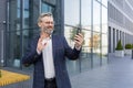 Successful mature man in business suit using app on phone for video call, senior businessman outside office building Royalty Free Stock Photo