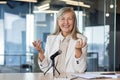 Successful middle aged woman sitting at desk with microphone and smiling while looking at camera. Confident senior Royalty Free Stock Photo