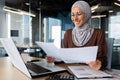 Successful muslim woman in hijab working inside office with documents, joyful financial accountant happy with reports Royalty Free Stock Photo