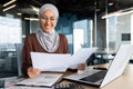 Successful muslim woman in hijab working inside office with documents, joyful financial accountant happy with reports Royalty Free Stock Photo