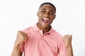 Successful pleased and happy handsome young african american guy in pink shirt clenching fists in victory and cheer