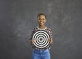 Successful positive african american woman holding a dart board standing on a gray background.