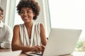 Successful project. Young and beautiful afro american woman working on laptop and looking away with smile while sitting Royalty Free Stock Photo