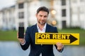 Successful real estate agent in a suit holding for rent sign near new apartment. Real estate agent with home loan Royalty Free Stock Photo
