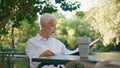 Successful senior reading newspaper on cafe terrace. Elegant woman rest in park Royalty Free Stock Photo