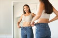 Successful slimming concept. Excited caucasian lady wearing jeans after weight loss, comparing size, posing near mirror Royalty Free Stock Photo