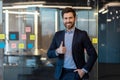 Successful and smiling young male businessman looking at camera and showing super sign with finger and holding hand in Royalty Free Stock Photo