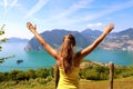 Successful sporty woman raising arms towards beautiful blue sky and lake. Female athlete celebrating sport success and goals.