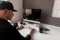 Successful stylish young photographer is working behind a computer in an office. Man in the cap sits at a table