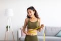 Successful weight loss. Slim Indian woman measuring waist with tape, satisfied with slimming program at home Royalty Free Stock Photo