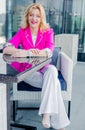 Successful woman entrepreneur in a magenta jacket posing on the terrace of a cafe in a business center. Royalty Free Stock Photo