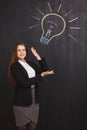 A young business woman has a great idea and raises her hands up pointing to a lightbulb on the board. Royalty Free Stock Photo