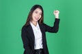 Successful young Asian business woman in suit raising hands and smiling on green isolated background