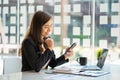 Successful young Asian businesswoman holding a smartphone working on a laptop computer financial graph data on the desk in the off Royalty Free Stock Photo