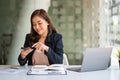Successful young Asian businesswoman holding a smartphone working on a laptop computer financial graph data on the desk in the off Royalty Free Stock Photo