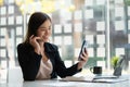 Successful young Asian businesswoman holding a smartphone working on a laptop computer financial graph data on the desk in the off Royalty Free Stock Photo