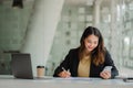 Successful young Asian businesswoman holding a smartphone working on a laptop computer financial graph data on the desk in the off Royalty Free Stock Photo