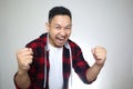 Successful young Asian man shows winning gesture, celebrating victory. Hands raised above with expressive wow happy face Royalty Free Stock Photo