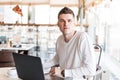 Successful young business man in a white shirt with a modern computer sits in a cafe. Cool freelancer guy working remotely Royalty Free Stock Photo