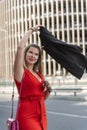 Successful young business woman in red dress swings jacket over her head. Vertical frame