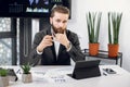 Successful young businessman in modern office pointing and looking directly at camera, while sitting at the table, using Royalty Free Stock Photo