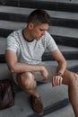 Successful young businessman in stylish shorts in suede brown shoes in a striped t-shirt with a leather bag looks at the clock. Royalty Free Stock Photo