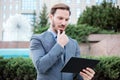 Successful young businessman working on a tablet in front of an office building. Holding hand on chin Royalty Free Stock Photo