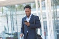 Successful young confident African American businessman moving with cellphone in hands against modern office building background Royalty Free Stock Photo