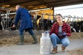 Successful girl farmer posing with milk can near stall with cows