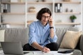 Successful young man talking on cellphone and taking notes, arranging job interview, sitting on sofa at home Royalty Free Stock Photo